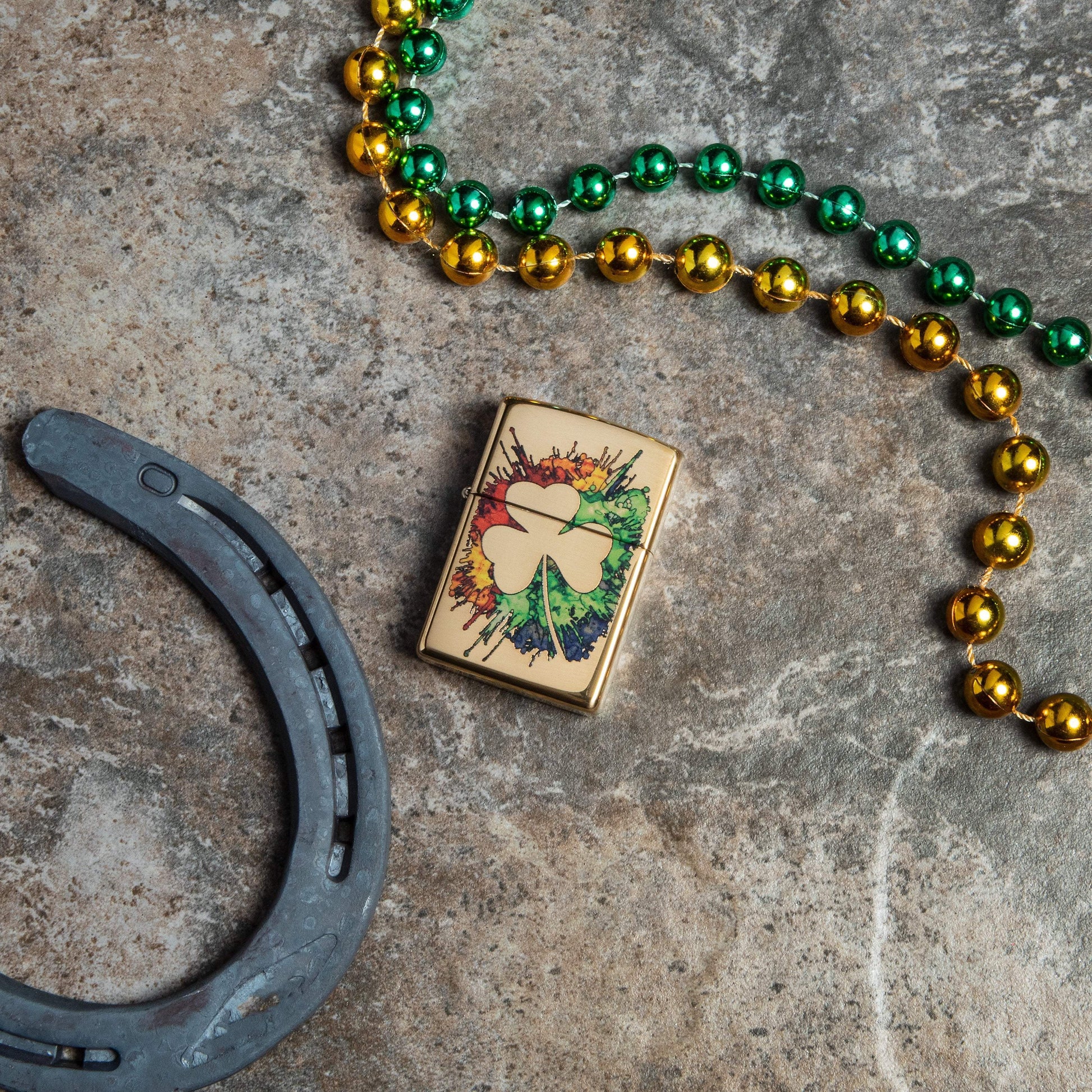 Lifestyle image of Graffiti Clover Design High Polish Brass Windproof Lighter laying next to a horseshoe and beads 