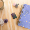 Lifestyle image of Starry Sky Design Iridescent Windproof Lighter laying flat on a desk with crystals and a sky themed planner