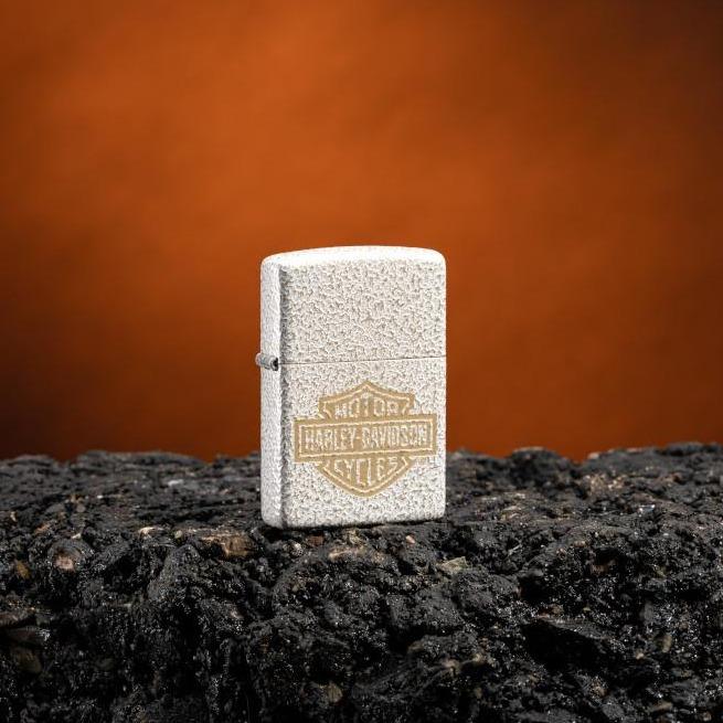 Lifestyle image of Harley-Davidson® Bar and Shield Logo Mercury Glass Windproof Lighter standing on asphalt with an orange background