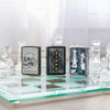 Lifestyle image of Chess Game Design Street Chrome™ Windproof Lighter standing with a Zippo themed lighter and a Skull lighter on a glass chess board with glass chess pieces.