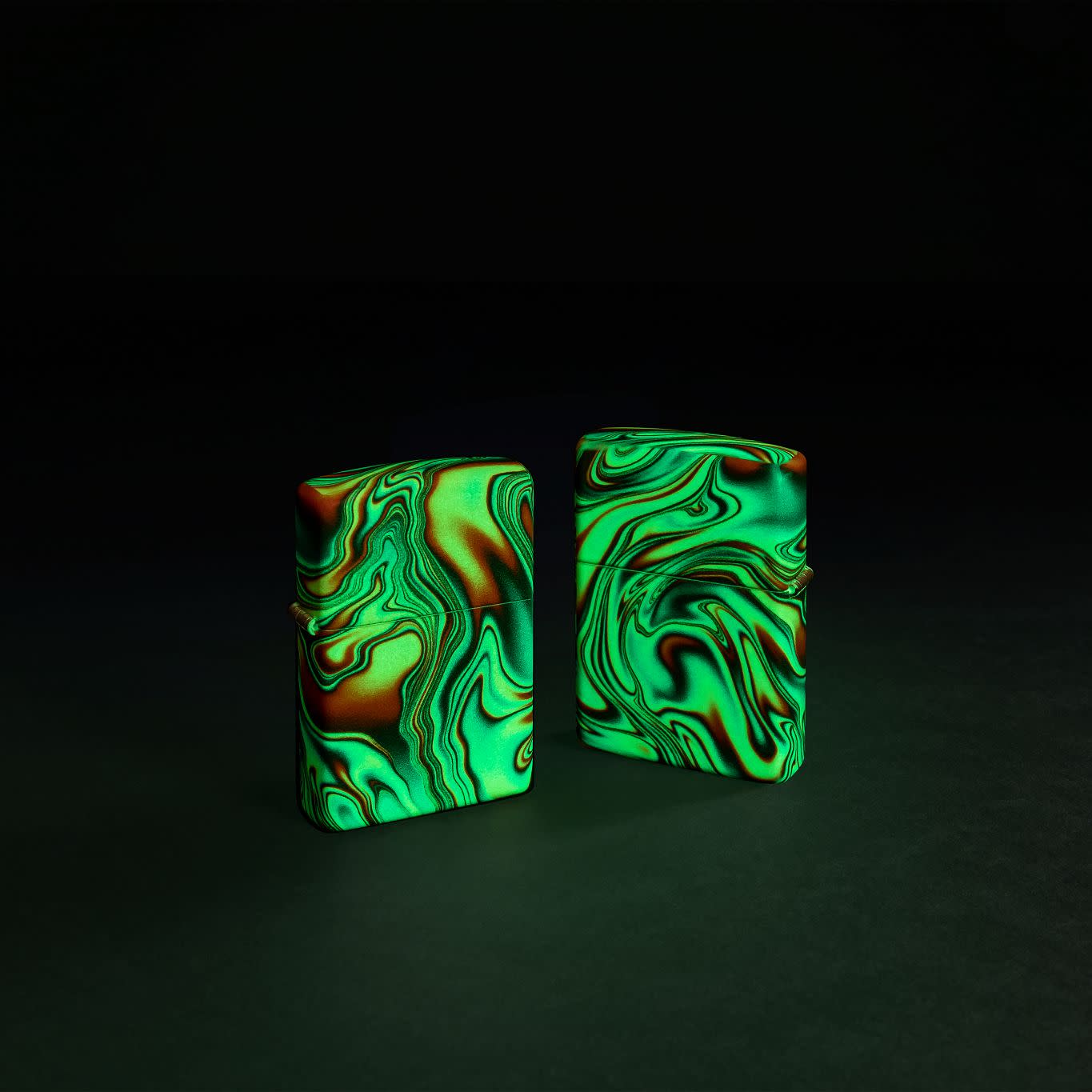 Glamour shot of two Zippo Colorful Swirl Design Glow in the Dark 540 Color Windproof Lighters, one showing the front and the other showing the back, glowing in the dark.