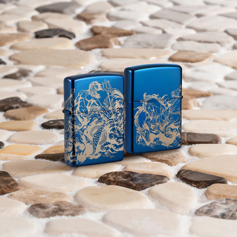 Lifestyle image of two Zippo Atlantis Design High Polish Blue Windproof Lighters standing on a sandy tiled surface.