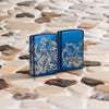 Lifestyle image of two Zippo Atlantis Design High Polish Blue Windproof Lighters standing on a sandy tiled surface.