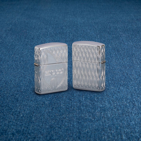 Lifestyle image of two Zippo Flame Design Armor High Polish Chrome Windproof Lighters standing on a denim surface.