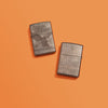 Lifestyle image of two Harley-Davidson Eagle Photo Image 360° High Polish Black Windproof Lighters laying on a orange background. One lighter is showing the front of the design, while the other shows the back.